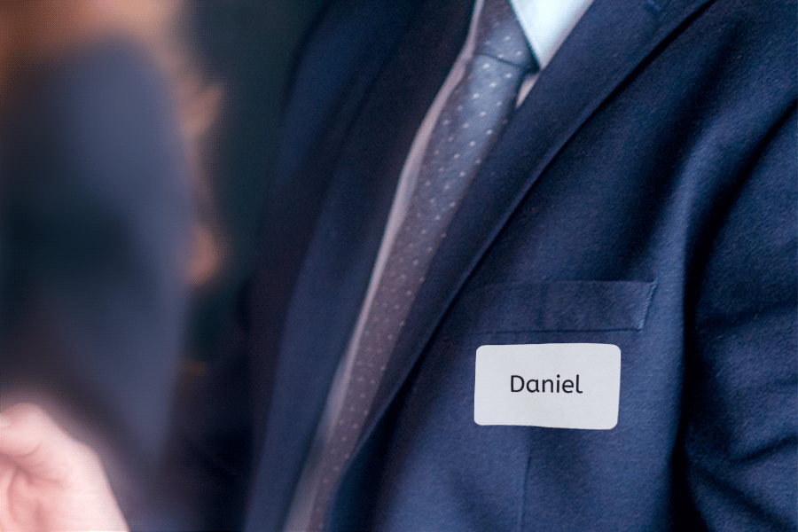 A man in a suit is wearing a name tag with the name 'Daniel' on the left side of his chest.