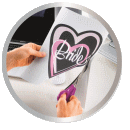 A person is cutting a paper heart with the word 'Bride' written on it with a pair of scissors.