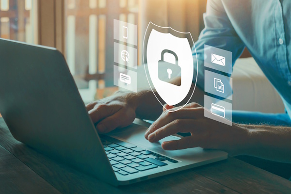 Eine Person tippt auf einem Laptop, während ein digitales Sicherheitssymbol mit einem Schloss und verschiedenen Icons für Internetdienste angezeigt wird.