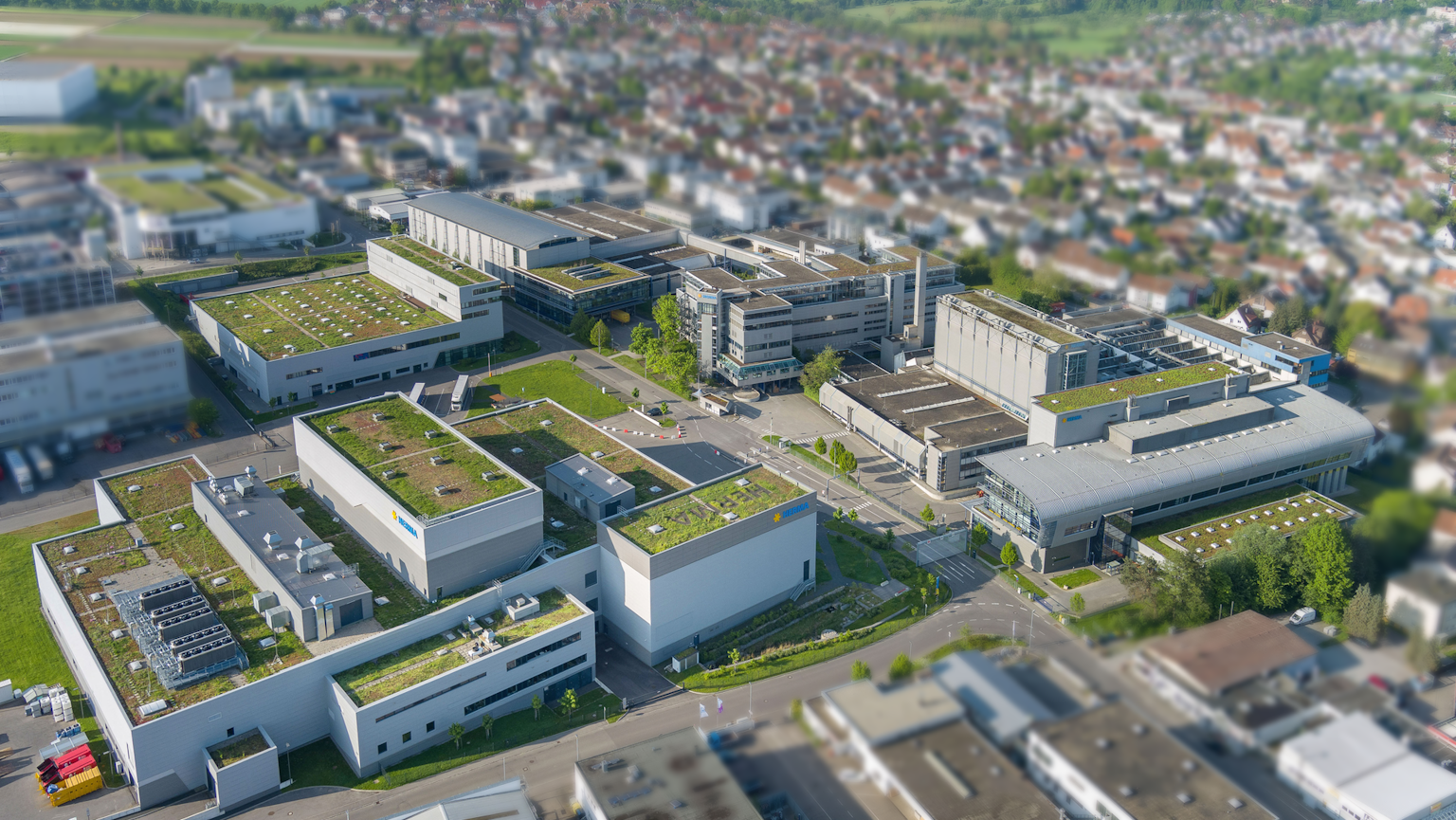 Aerial view of a modern commercial area featuring several buildings with green roofs, surrounded by an urban landscape.