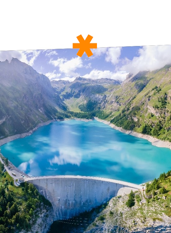A clear reservoir surrounded by mountains and forests, with a concrete wall in the foreground holding back the water.