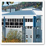 Modern buildings with large windows and blue accents, surrounded by trees and hills in the background.
