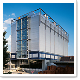 Modern, multi-story buildings with glass facades and blue accents, surrounded by trees and a storage area in the foreground.