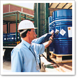 A worker in a hard hat scans a label on a blue barrel during the receiving process at a truck.