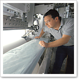 A man is working on a machine that processes a long, transparent film. He is focused on the process.