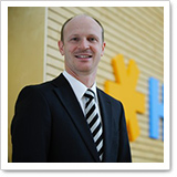 Man in a suit and tie, smiling in front of a wall with colorful letters.