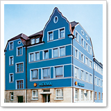 Blue building with several windows and an entrance labeled 'HITRIVA.' The roof has a distinctive shape.