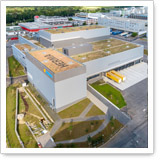 Aerial view of a modern building with a green roof, surrounded by pathways and green spaces, in an industrial setting.