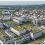 Aerial view of a modern urban area with several buildings and green roofs, surrounded by a rural landscape.