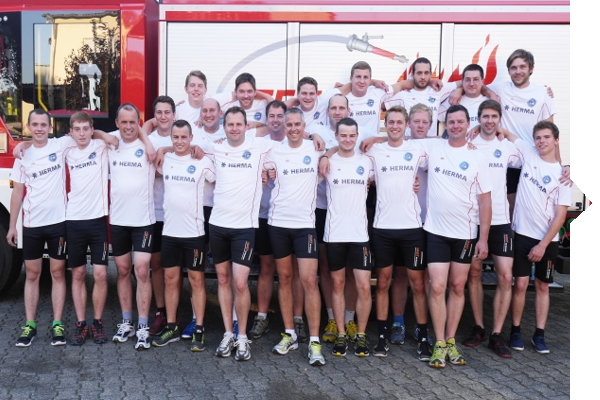 A group of 22 men in white T-shirts and shorts stands in front of a fire truck, posing together for a group photo.