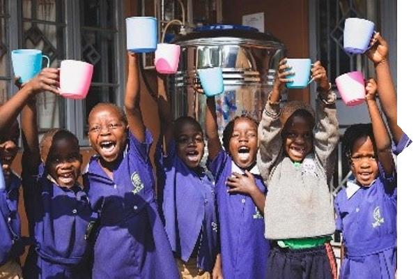 A group of children in blue school uniforms happily raises colorful cups in the air as they stand in front of a water container.