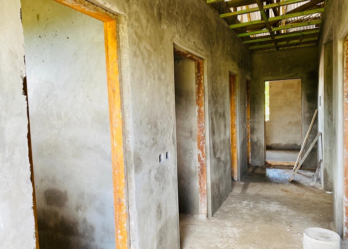 A partially finished hallway with several open doors and a concrete floor, surrounded by bare walls and a visible roof structure.