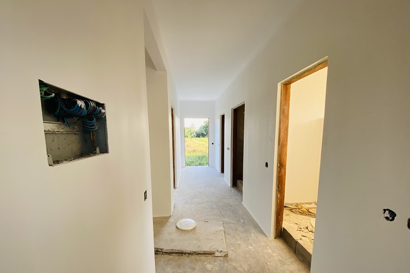 A bright hallway with white walls, open doors leading to other rooms, and a view of a green outdoor area.