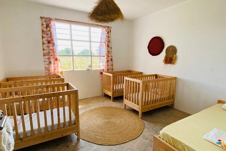 A bright room with four wooden children's beds, a round rug, and colorful curtains. A window offers a view outside.