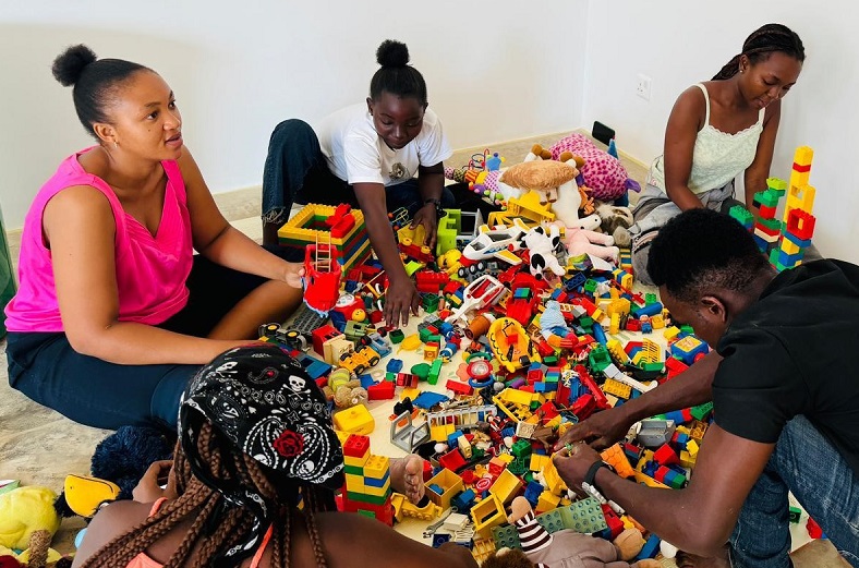 A group of five people is sitting on the floor, playing with colorful building blocks and toys.