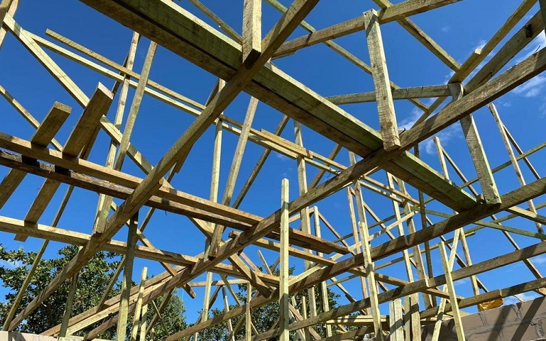 Wooden frame construction under a blue sky, with visible beams and supports that uphold the structure of a building.
