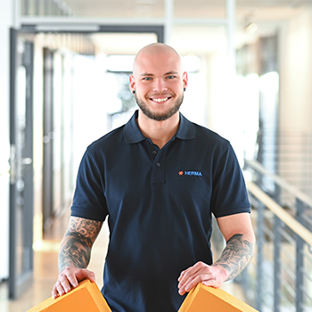 A bald man is wearing a dark blue polo shirt and holding two orange objects in his hands.