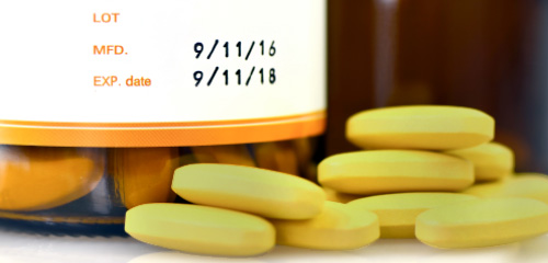Yellow tablets are next to a small bottle with a label showing the manufacturing date and the expiration date.