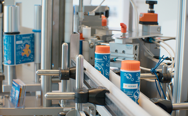 Machines for filling bottles with orange caps on a conveyor belt in a production environment.