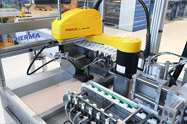 Industrial robot with a yellow arm working on an automated machine to assemble or move components.