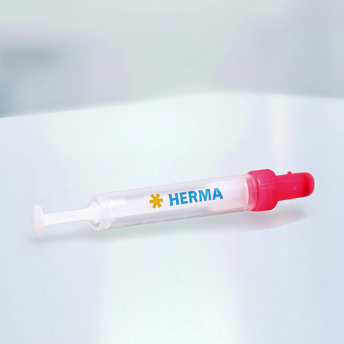 A syringe with a red cap and the label 'HERMA' on a light background.