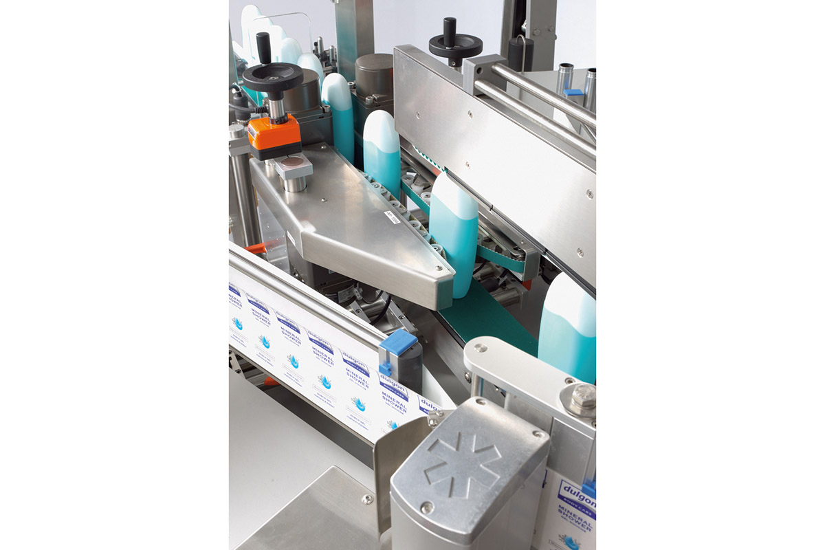An industrial packaging machine with bottles placed on a conveyor belt and various mechanical components for labeling.