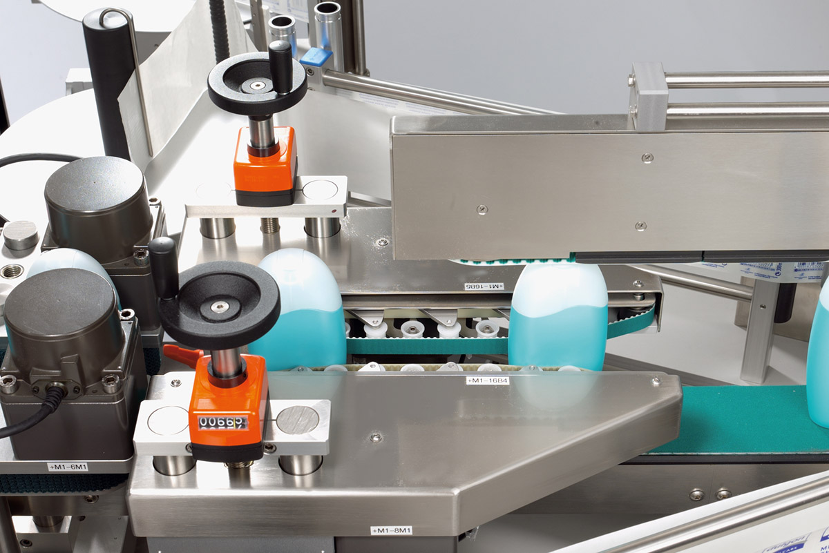 Machines for filling liquids, with bottles in blue and white on a conveyor belt.