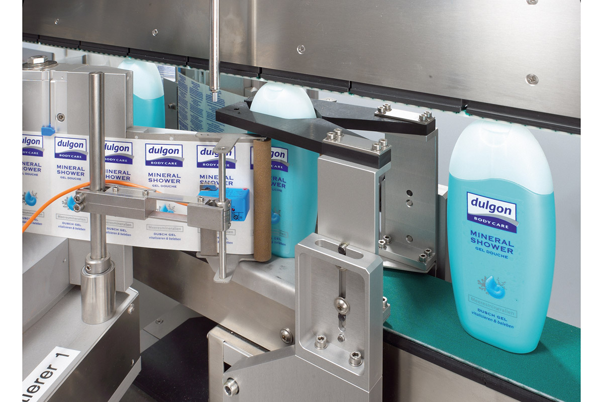 A bottle of Dulgon Mineral Shower is on a conveyor belt, surrounded by packaging. Machine components are visible.