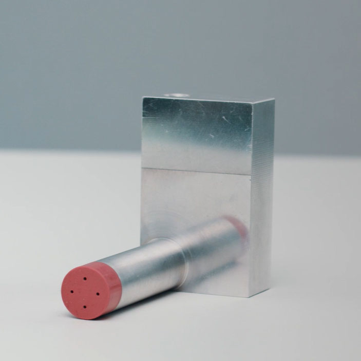 A silver cylinder with a red end lies next to a rectangular silver block. Both objects have a smooth surface.