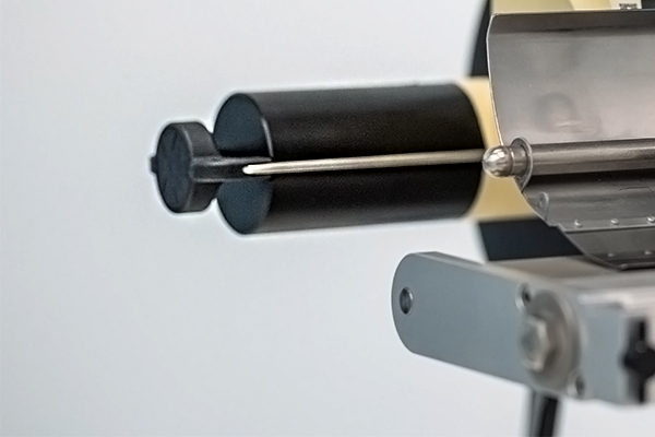 Close-up of a device with two rollers and a needle, used for precise applications in manufacturing or engineering.