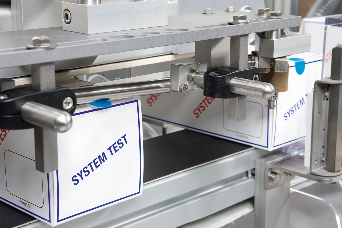 Machine for packaging with boxes labeled 'SYSTEM TEST.' Mechanical parts are visible.