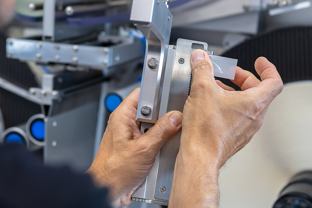 A person is adjusting a precise measuring instrument with both hands while working on a technical machine.