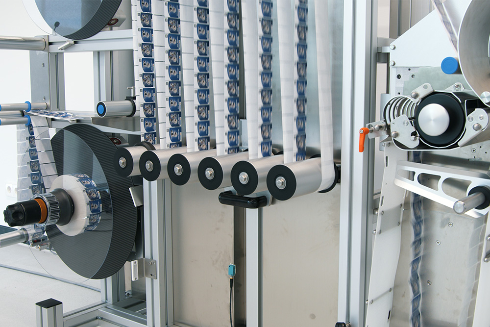 Machine for processing strips, featuring multiple rollers and a mechanical system for arranging the materials.