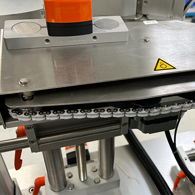 A machine component with an orange element, metal surfaces, and a chain drive, mounted in an industrial setting.