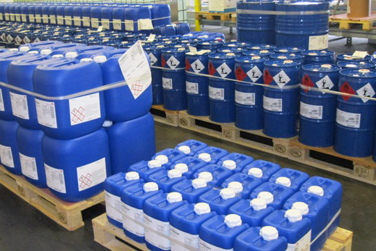 GHS labels and chemical labels on blue plastic containers, on pallets.