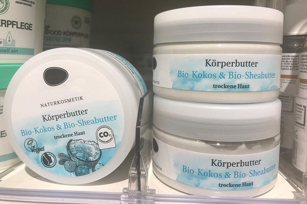 White cream jar with natural cosmetics body butter on the shelf, labeled on the lid and body with colorful blue and white printed labels.
