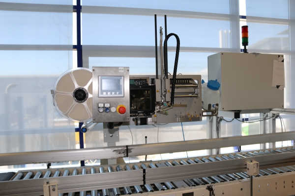 HERMA InNo-Liner: HERMA InNo-Liner labeling machine in front of a glass panel