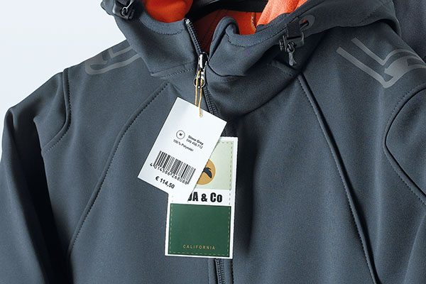 Colorfully printed tags with price and product labeling, attached to a gray softshell jacket.