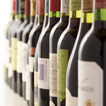 A row of wine bottles with various labels standing on a table. The bottles are arranged in different colors and shapes.