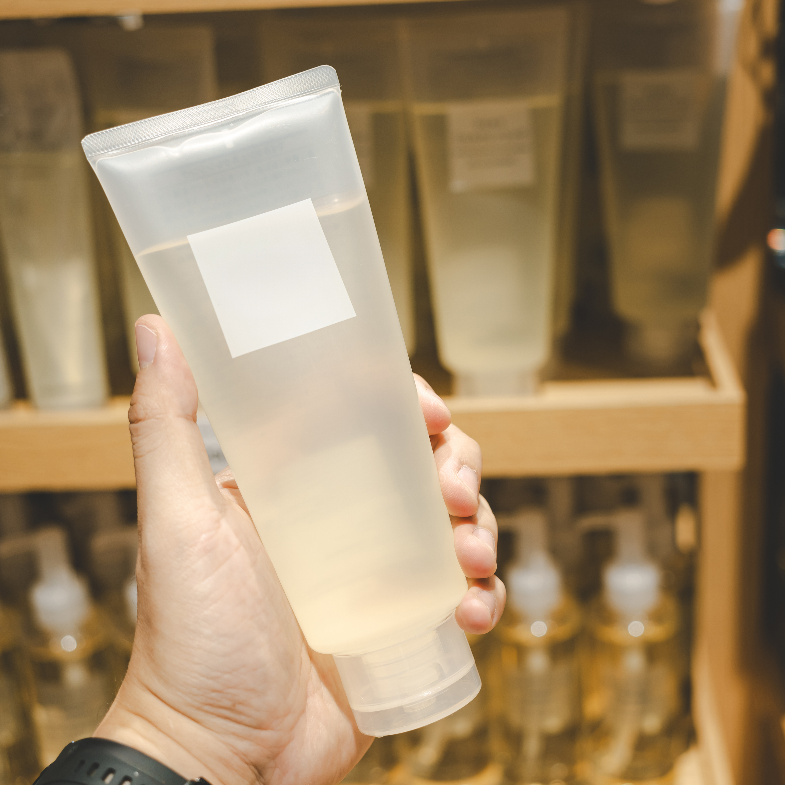 A hand holds a transparent tube with an unlabelled sticker, surrounded by other similar products in the background.