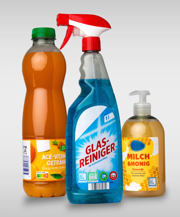 Three bottles are lined up next to each other: an orange drink bottle, a blue glass cleaner spray bottle, and a bottle of milk and honey soap.