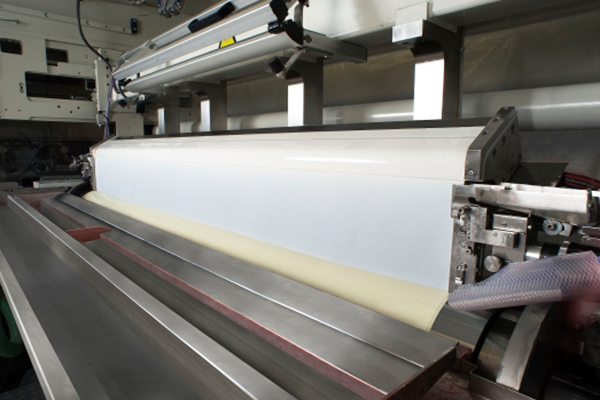 An industrial machine that processes a long, flat sheet of dough, with a focus on the production process.
