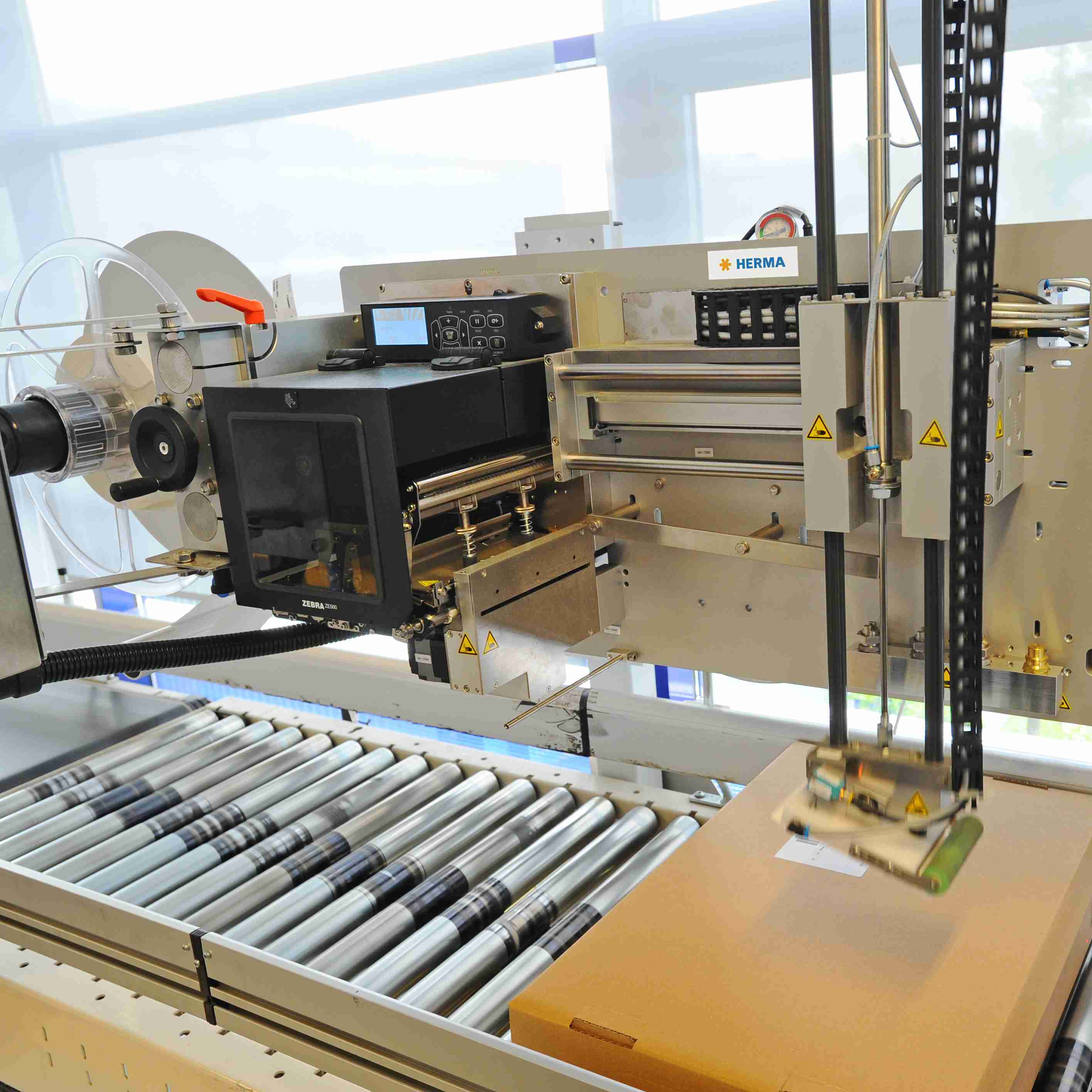 Automated labeling machine with a conveyor belt and control unit that labels boxes.