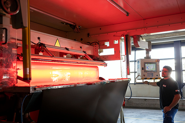 A worker operates a machine in a production hall, while a red light is flashing from the machine.