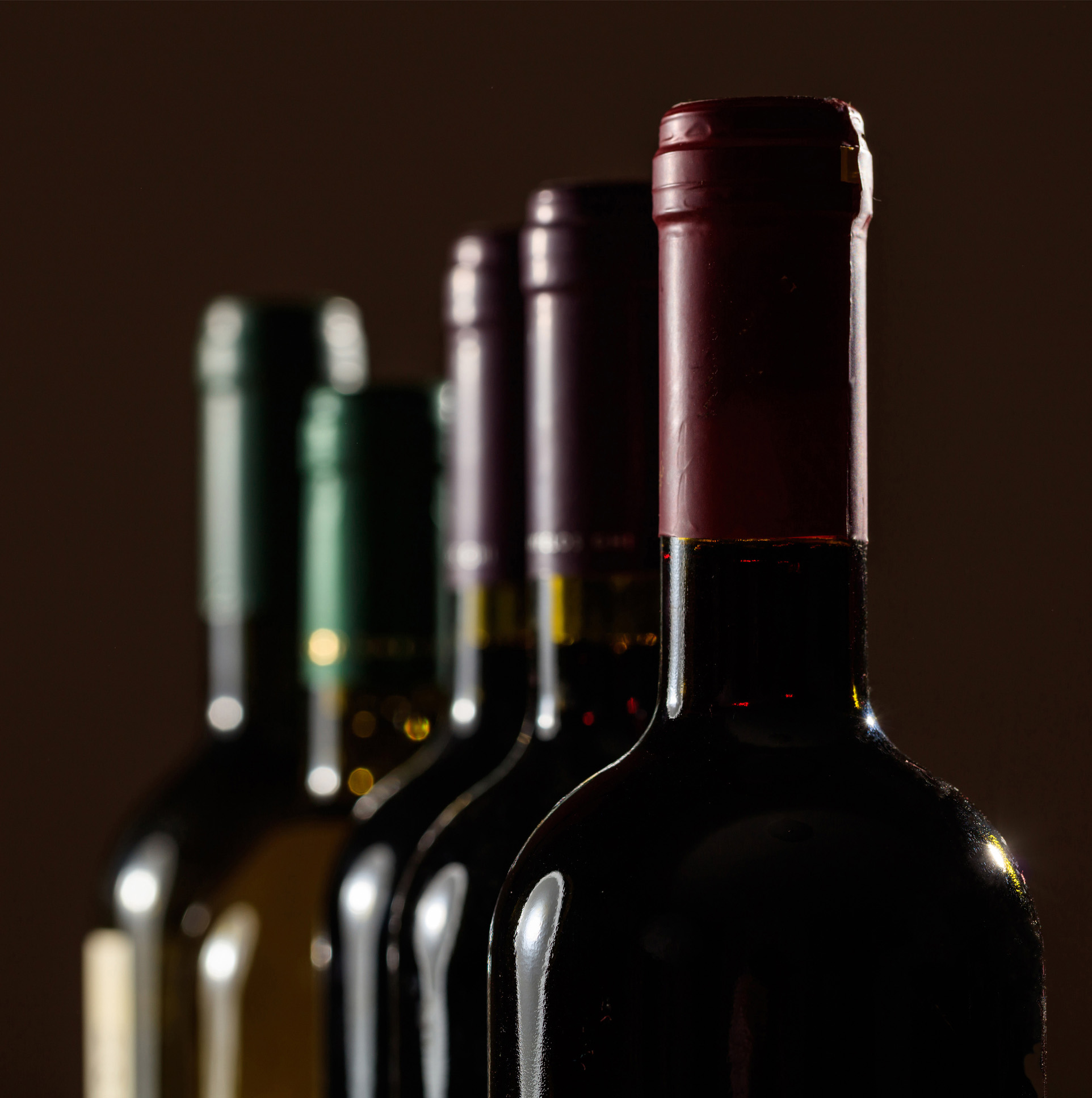 Five wine bottles with different colored caps are lined up, partially blurred in the background.