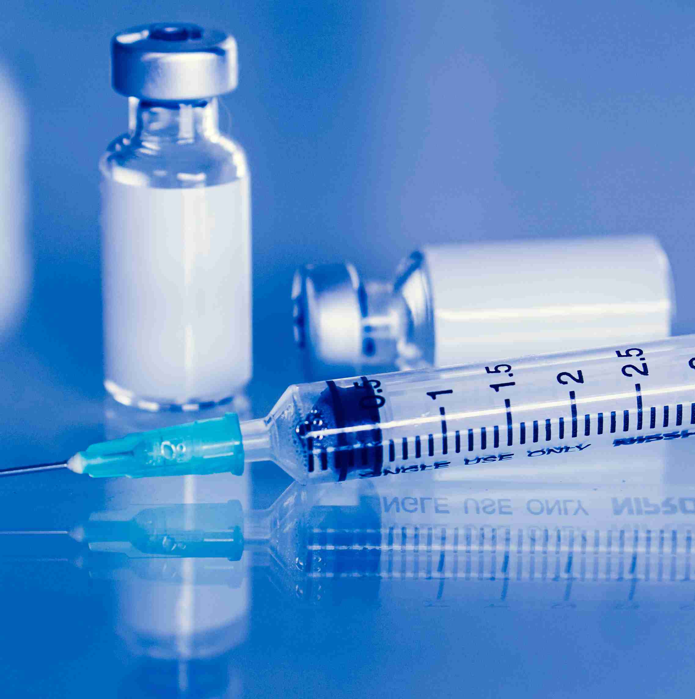 Injection with a needle and two glass vials containing clear liquid on a reflective surface.