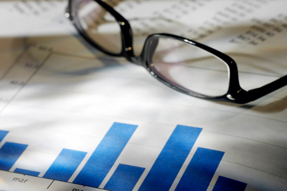 Blue bar charts on a document, next to them are a pair of glasses and additional printed data.