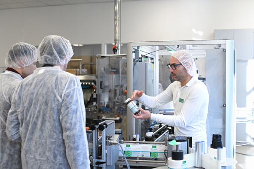 A staff member is explaining to a group of people in protective gear how to use a container in a production environment.