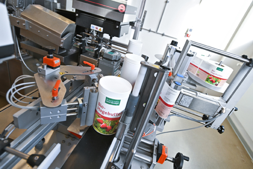 Machine for filling organic butter into containers, featuring various mechanical components and labeling stations.