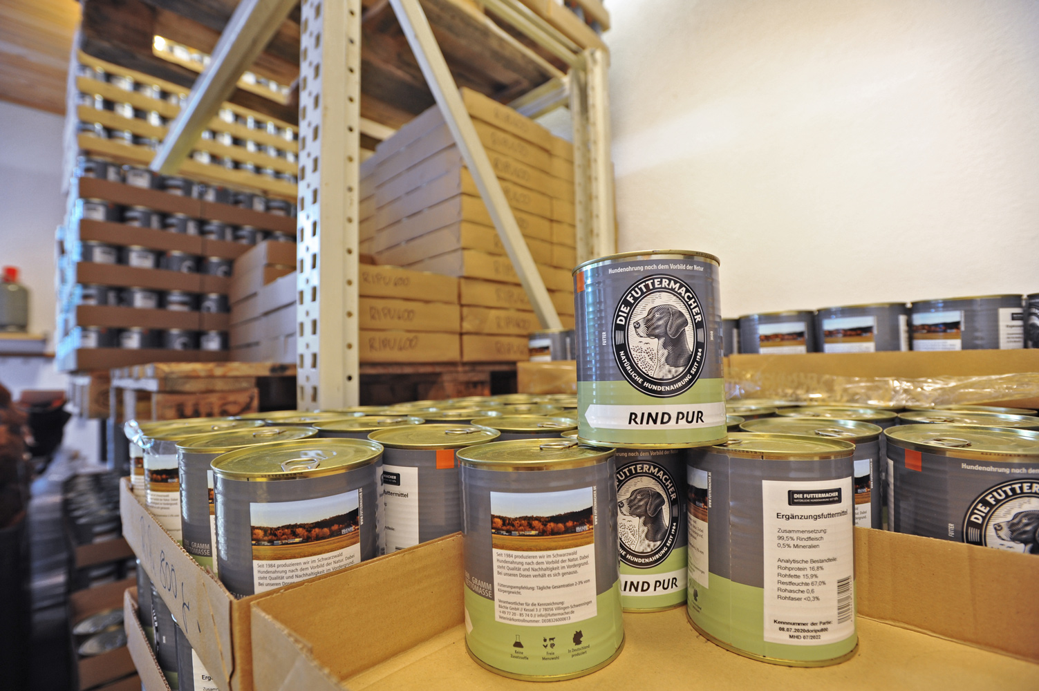 Canned beef is sitting on a shelf in a storage room. In the background, more shelves and wooden pallets are visible.